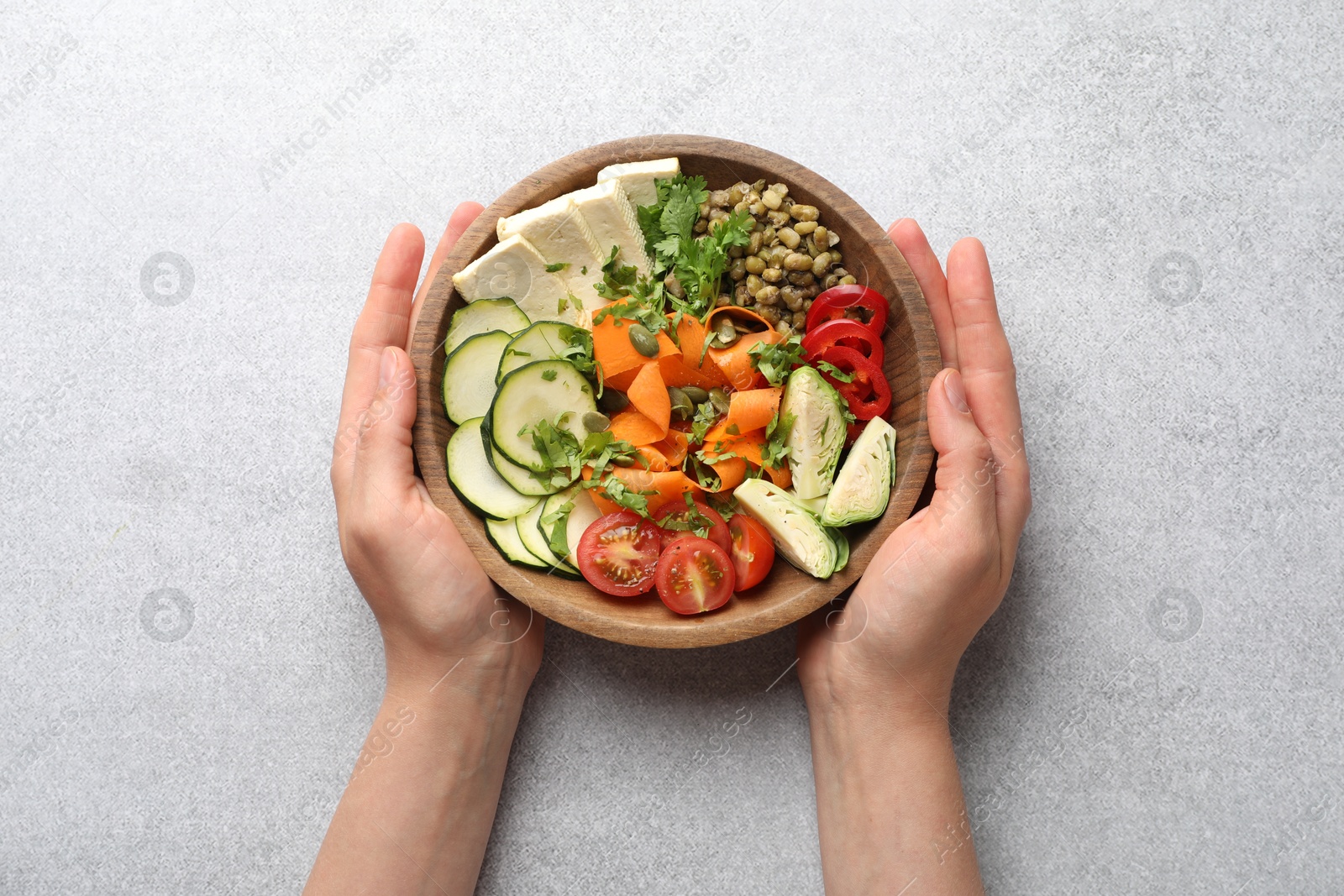 Healthy vegetarian food. Woman with delicious Buddha bowl at light grey table, top view Photo of Healthy vegetarian food. Woman with delicious Buddha bowl at light grey table, top view