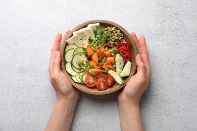 Photo of Healthy vegetarian food. Woman with delicious Buddha bowl at light grey table, top view