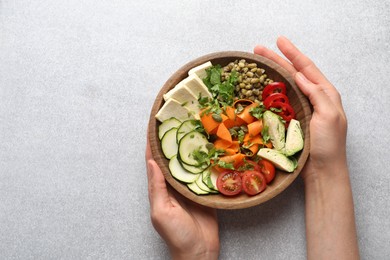 Photo of Healthy vegetarian food. Woman with delicious Buddha bowl at light grey table, top view. Space for text