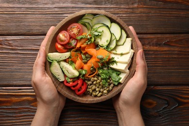 Photo of Healthy vegetarian food. Woman with delicious Buddha bowl at wooden table, top view