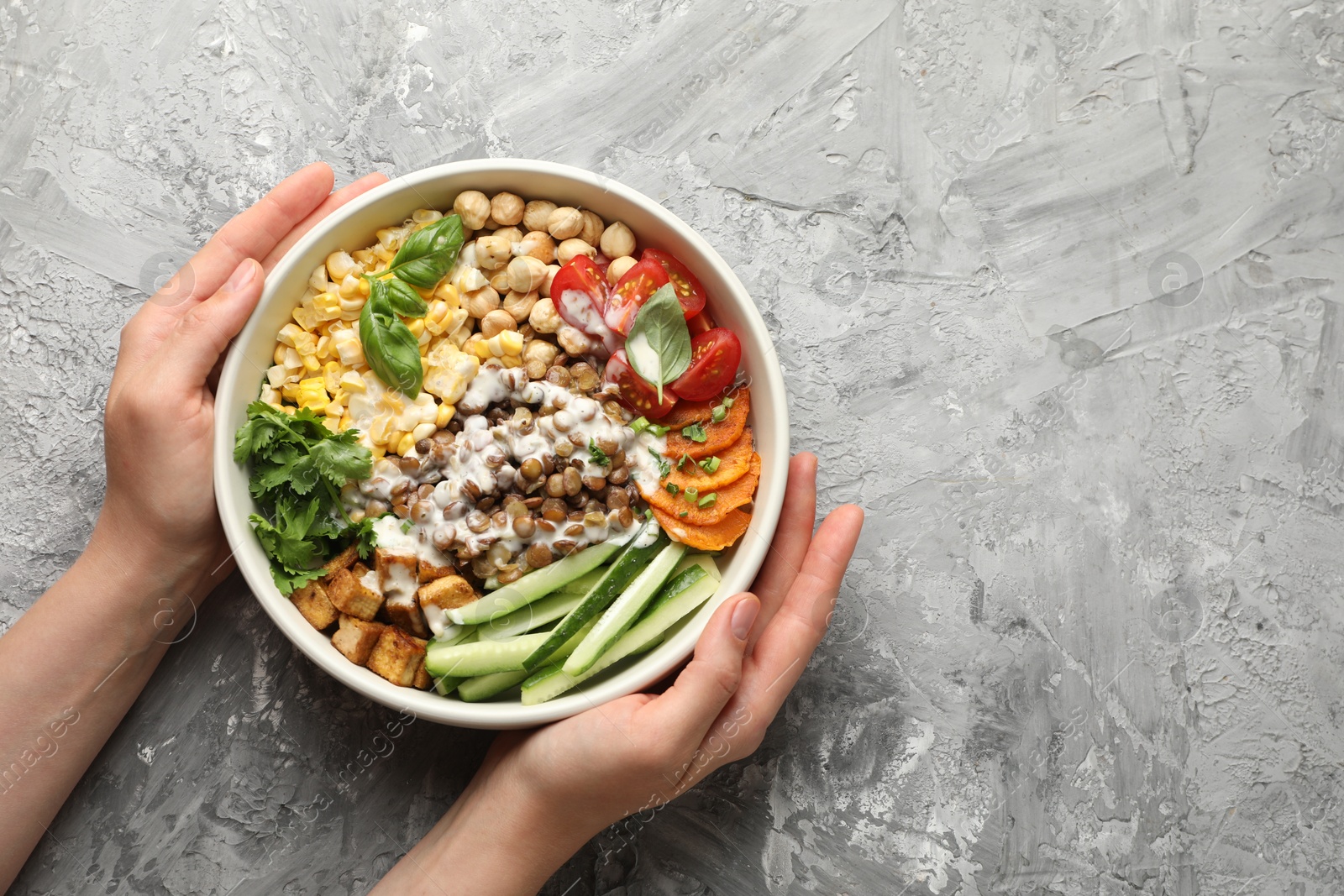 Healthy vegetarian food. Woman with delicious Buddha bowl at grey table, top view. Space for text Photo of Healthy vegetarian food. Woman with delicious Buddha bowl at grey table, top view. Space for text