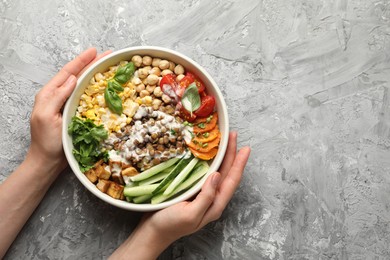 Photo of Healthy vegetarian food. Woman with delicious Buddha bowl at grey table, top view. Space for text