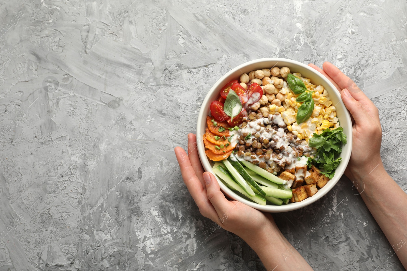 Healthy vegetarian food. Woman with delicious Buddha bowl at grey table, top view. Space for text Photo of Healthy vegetarian food. Woman with delicious Buddha bowl at grey table, top view. Space for text