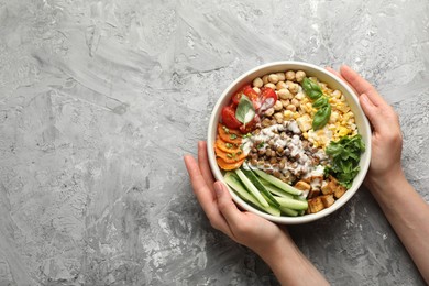 Photo of Healthy vegetarian food. Woman with delicious Buddha bowl at grey table, top view. Space for text