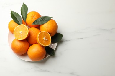 Photo of Fresh oranges and leaves on white marble table, top view. Space for text