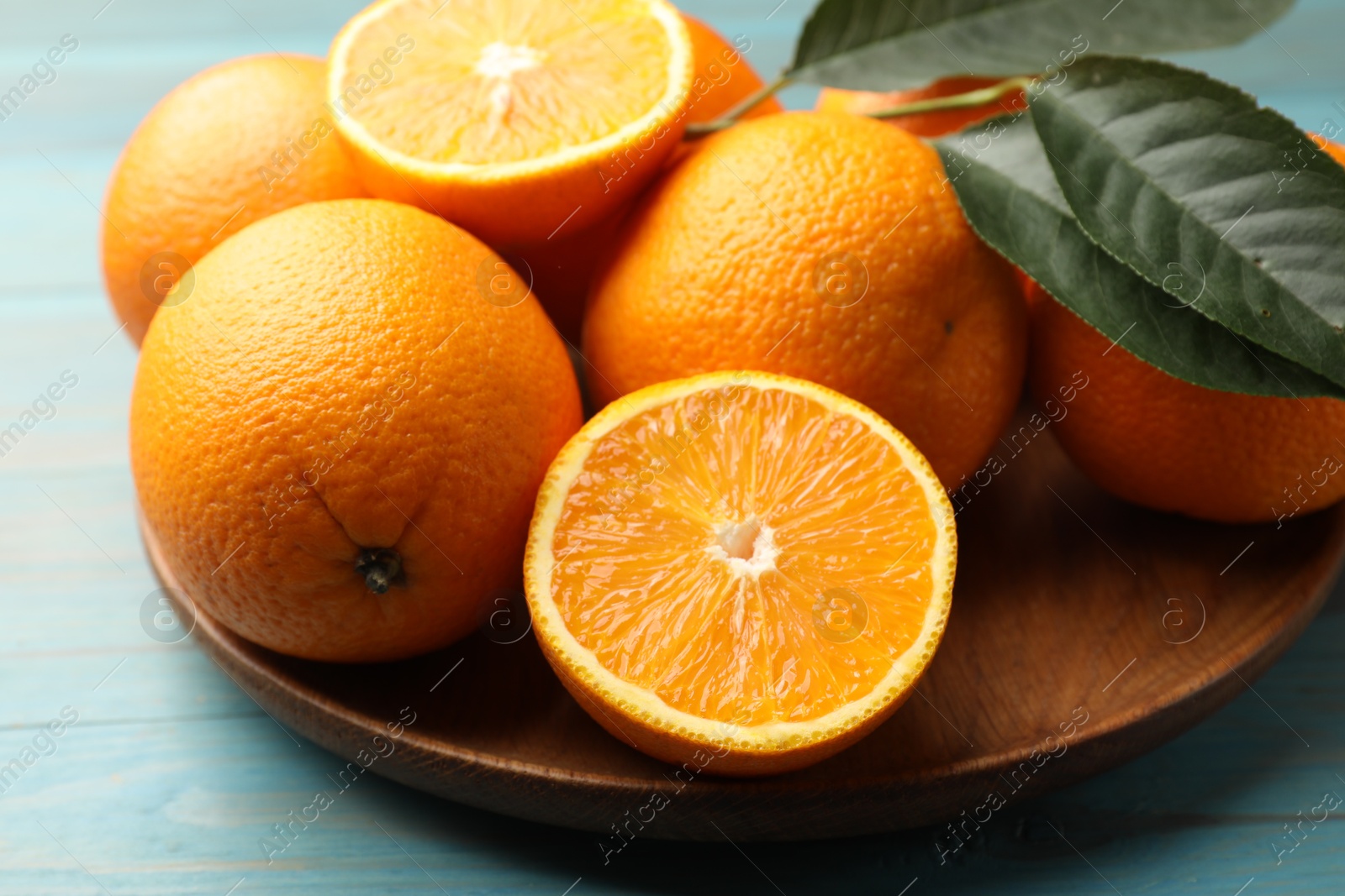 Fresh oranges and leaves on light blue wooden table, closeup Photo of Fresh oranges and leaves on light blue wooden table, closeup
