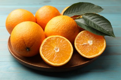 Photo of Fresh oranges and leaves on light blue wooden table, closeup