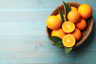 Photo of Fresh oranges and leaves in wicker basket on light blue wooden table, top view. Space for text