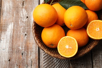 Photo of Fresh oranges and leaves in wicker basket on wooden table, top view. Space for text