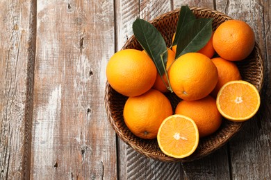 Photo of Fresh oranges and leaves in wicker basket on wooden table, top view. Space for text