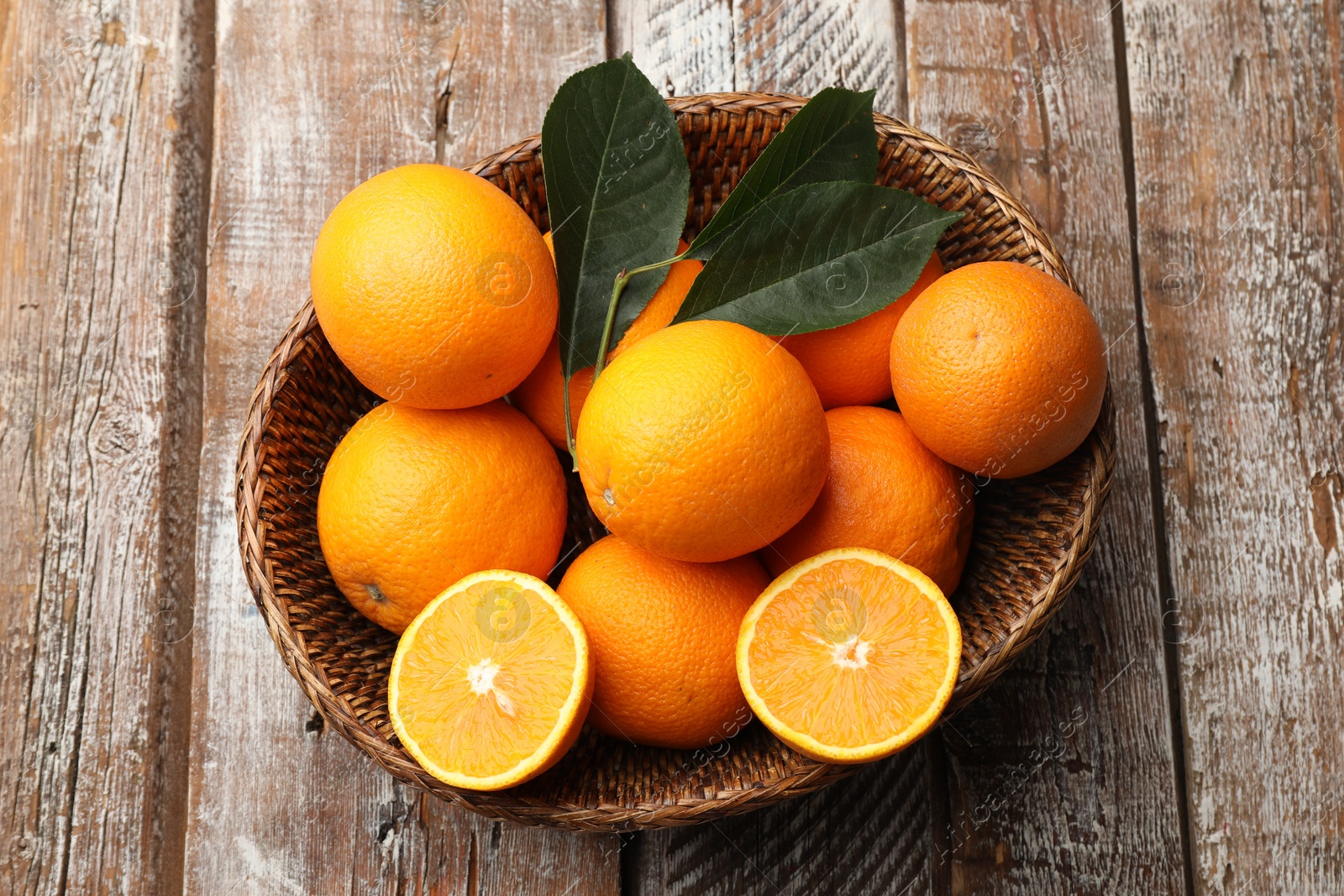 Fresh oranges and leaves in wicker basket on wooden table, top view Photo of Fresh oranges and leaves in wicker basket on wooden table, top view
