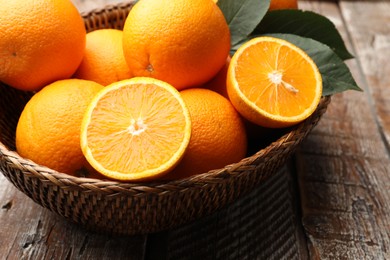 Photo of Fresh oranges and leaves in wicker basket on wooden table, closeup