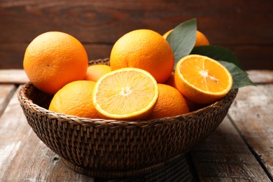 Photo of Fresh oranges and leaves in wicker basket on wooden table, closeup