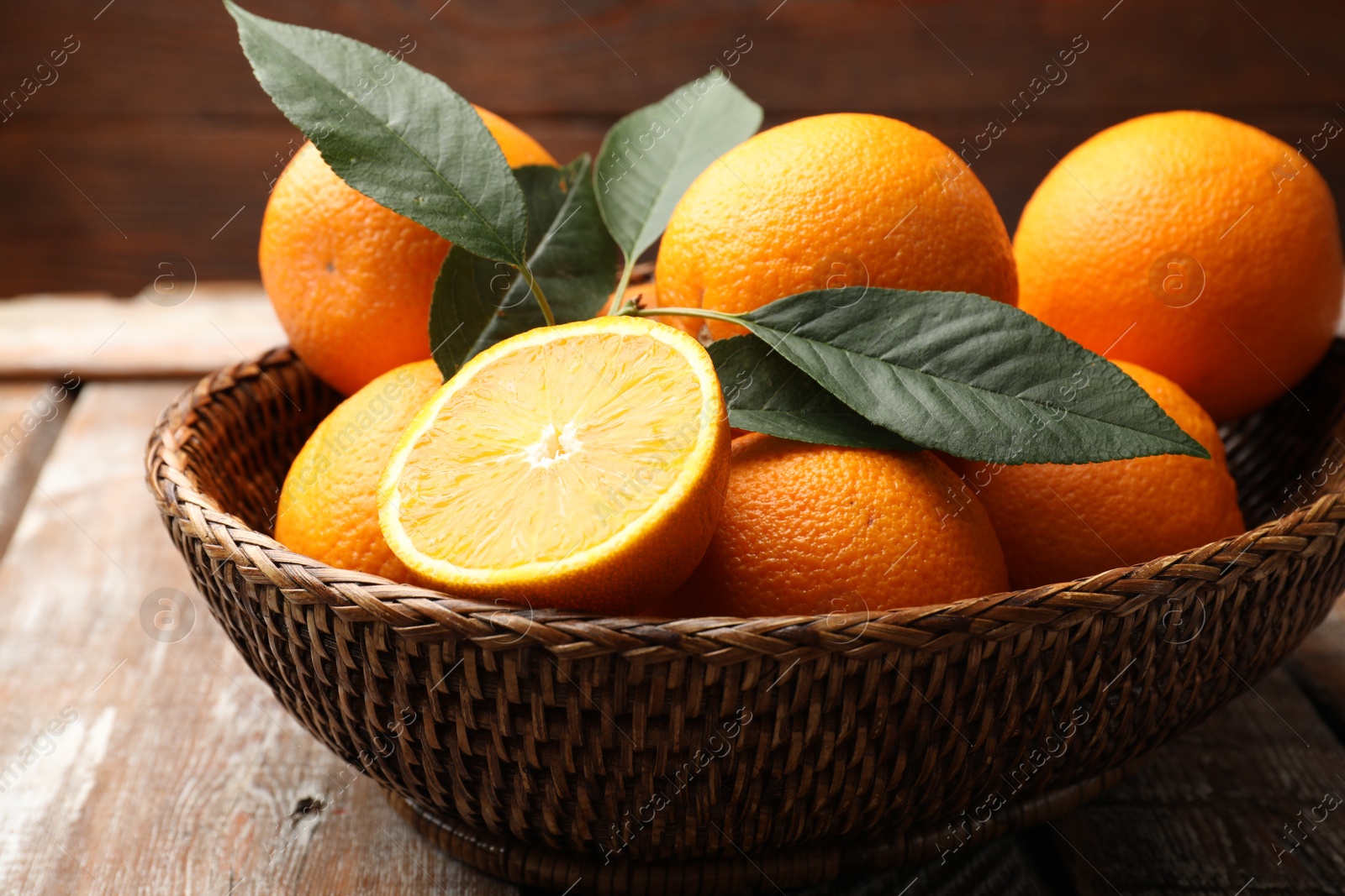 Fresh oranges and leaves in wicker basket on wooden table, closeup Photo of Fresh oranges and leaves in wicker basket on wooden table, closeup