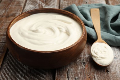 Photo of Delicious sour cream in bowl and spoon on wooden table, closeup