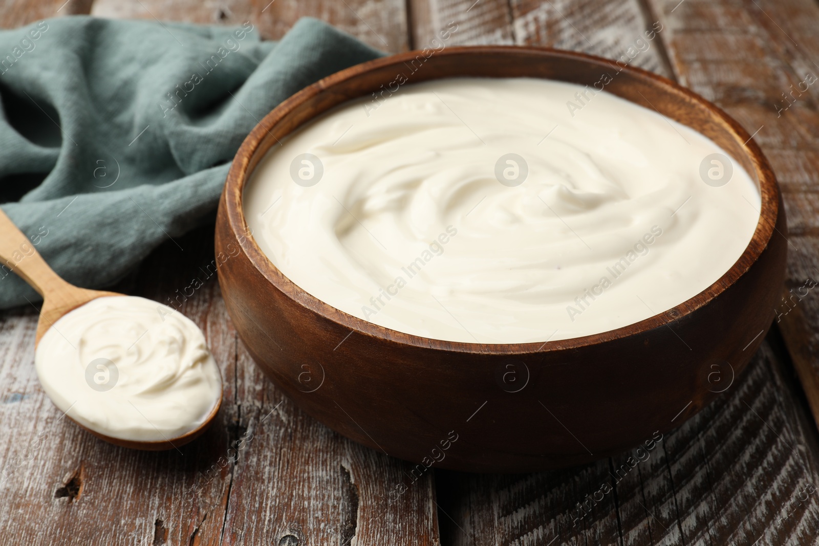 Delicious sour cream in bowl and spoon on wooden table, closeup Photo of Delicious sour cream in bowl and spoon on wooden table, closeup