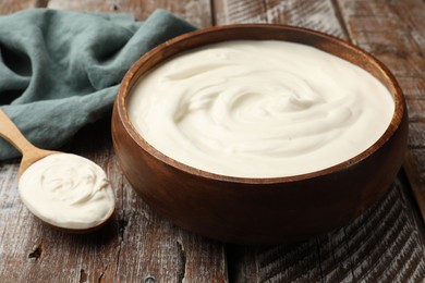 Photo of Delicious sour cream in bowl and spoon on wooden table, closeup