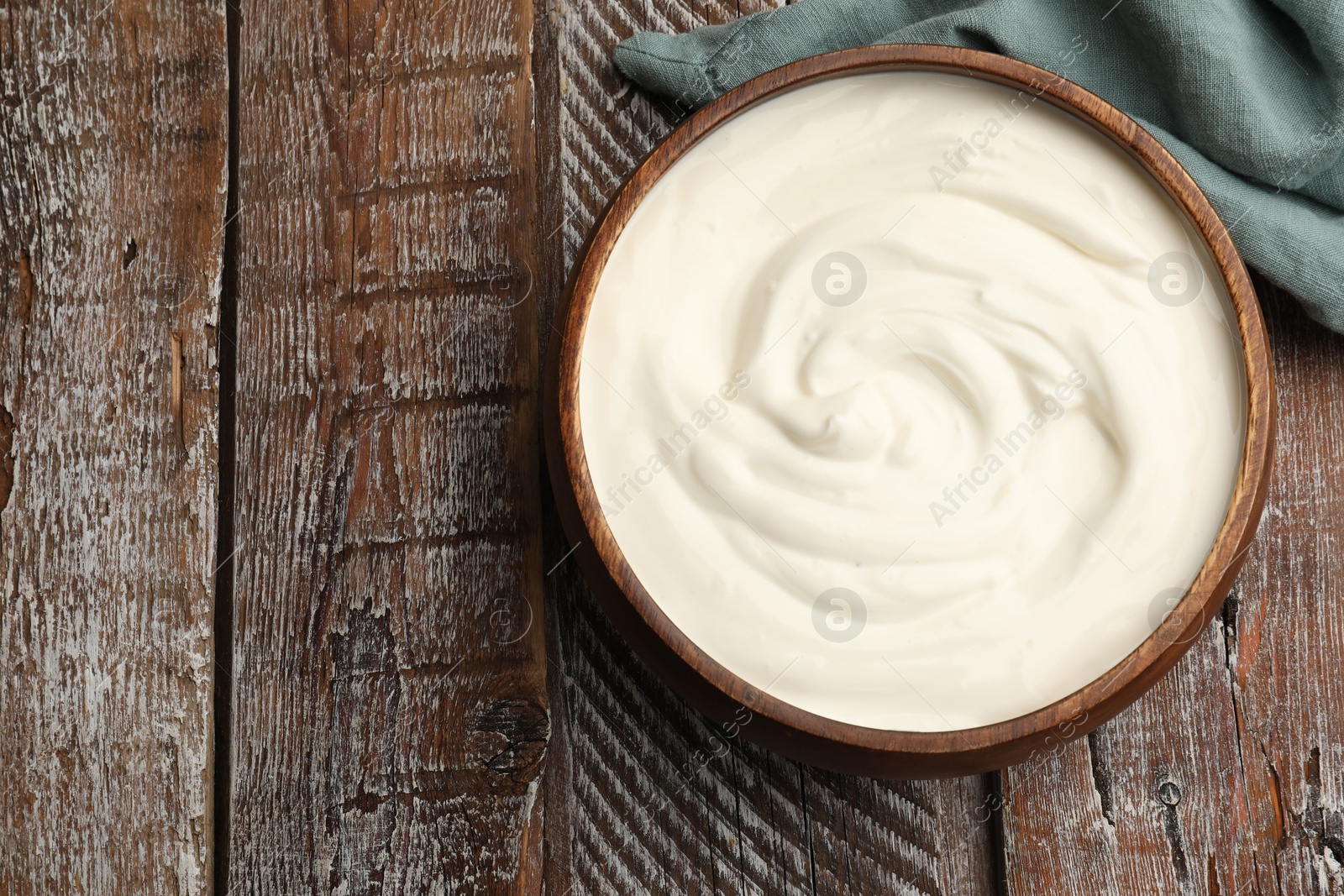 Photo of Delicious sour cream in bowl on wooden table, top view. Space for text