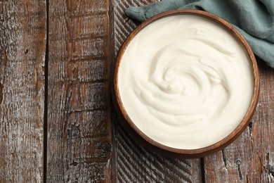 Photo of Delicious sour cream in bowl on wooden table, top view. Space for text