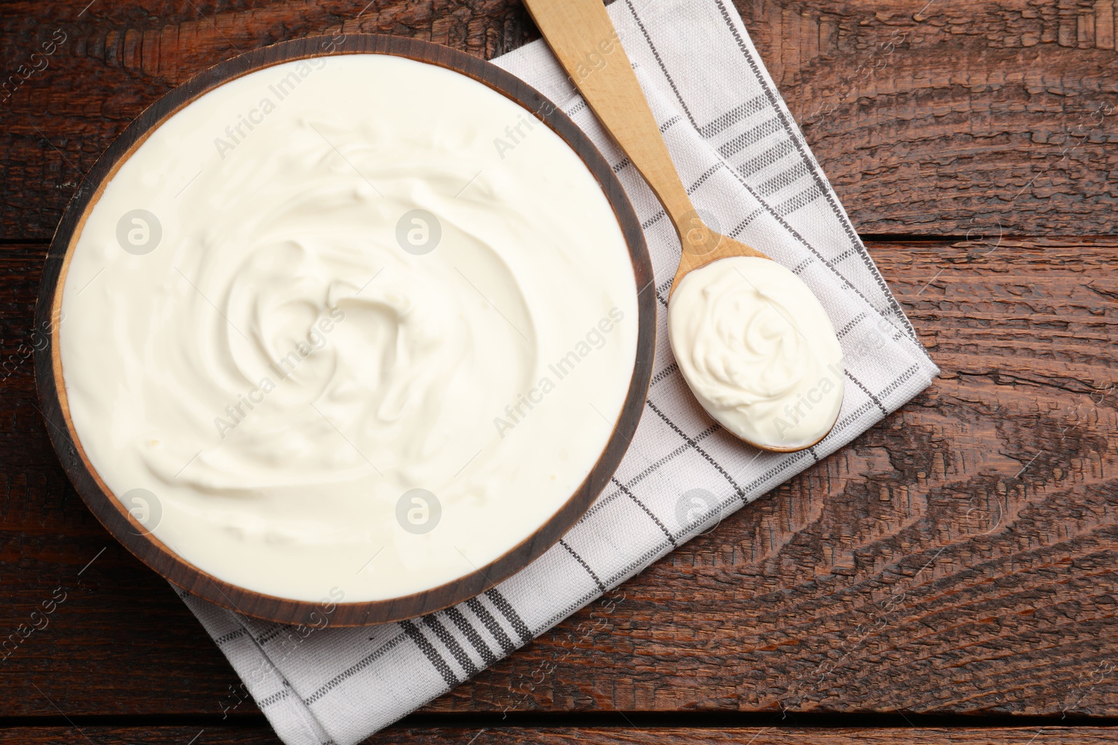 Delicious sour cream in bowl and spoon on wooden table, top view Photo of Delicious sour cream in bowl and spoon on wooden table, top view