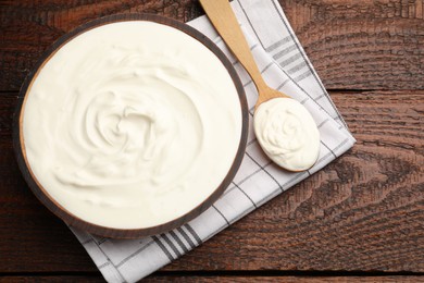 Photo of Delicious sour cream in bowl and spoon on wooden table, top view