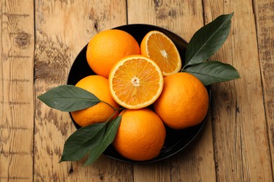 Photo of Fresh ripe oranges and leaves on wooden table, top view