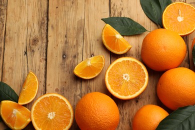 Photo of Fresh ripe oranges and leaves on wooden table, flat lay. Space for text