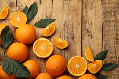 Photo of Fresh ripe oranges and leaves on wooden table, flat lay. Space for text