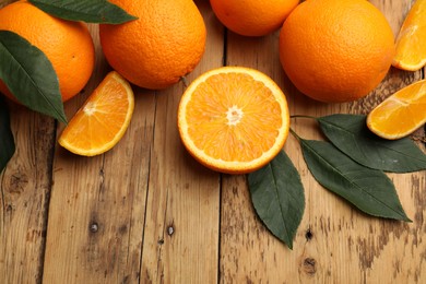 Photo of Fresh ripe oranges and leaves on wooden table, flat lay. Space for text