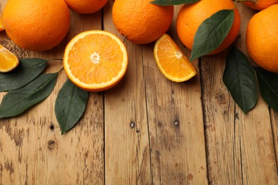 Photo of Fresh ripe oranges and leaves on wooden table, flat lay. Space for text