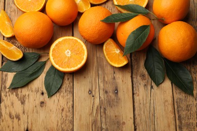 Photo of Fresh ripe oranges and leaves on wooden table, flat lay. Space for text