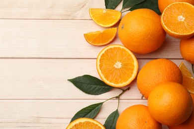 Photo of Fresh ripe oranges and leaves on light wooden table, flat lay. Space for text