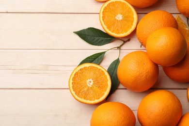 Photo of Fresh ripe oranges and leaves on light wooden table, flat lay. Space for text