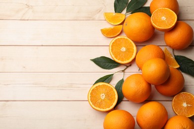 Photo of Fresh ripe oranges and leaves on light wooden table, flat lay. Space for text