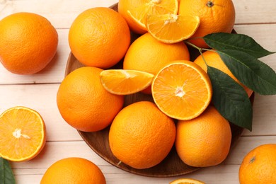 Photo of Fresh ripe oranges and leaves on light wooden table, flat lay