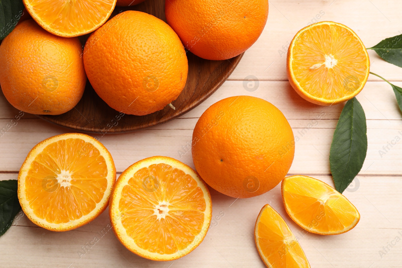 Fresh ripe oranges and leaves on light wooden table, flat lay Photo of Fresh ripe oranges and leaves on light wooden table, flat lay