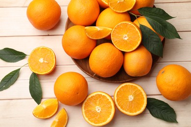 Photo of Fresh ripe oranges and leaves on light wooden table, flat lay