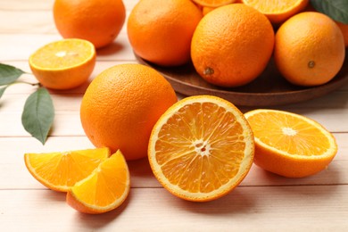 Photo of Fresh ripe oranges and leaves on light wooden table, closeup