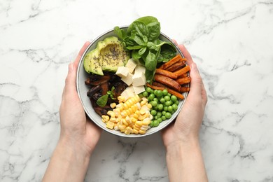 Photo of Healthy vegetarian food. Woman with delicious Buddha bowl at white marble table, top view