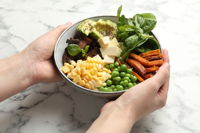 Photo of Healthy vegetarian food. Woman with delicious Buddha bowl at white marble table, closeup