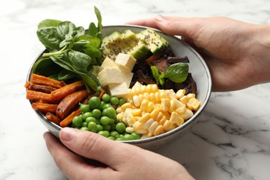 Photo of Healthy vegetarian food. Woman with delicious Buddha bowl at white marble table, closeup