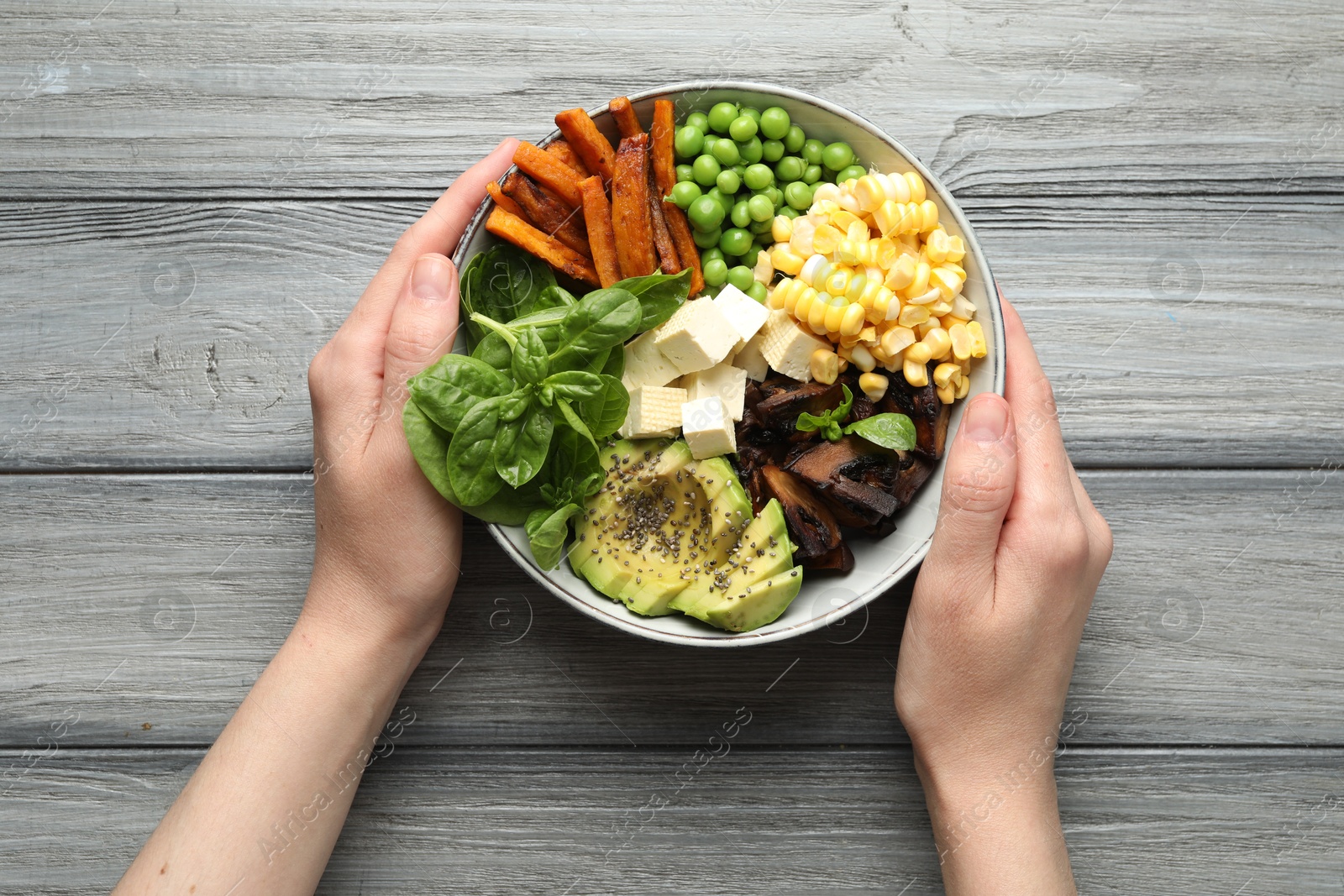 Healthy vegetarian food. Woman with delicious Buddha bowl at grey wooden table, top view Photo of Healthy vegetarian food. Woman with delicious Buddha bowl at grey wooden table, top view