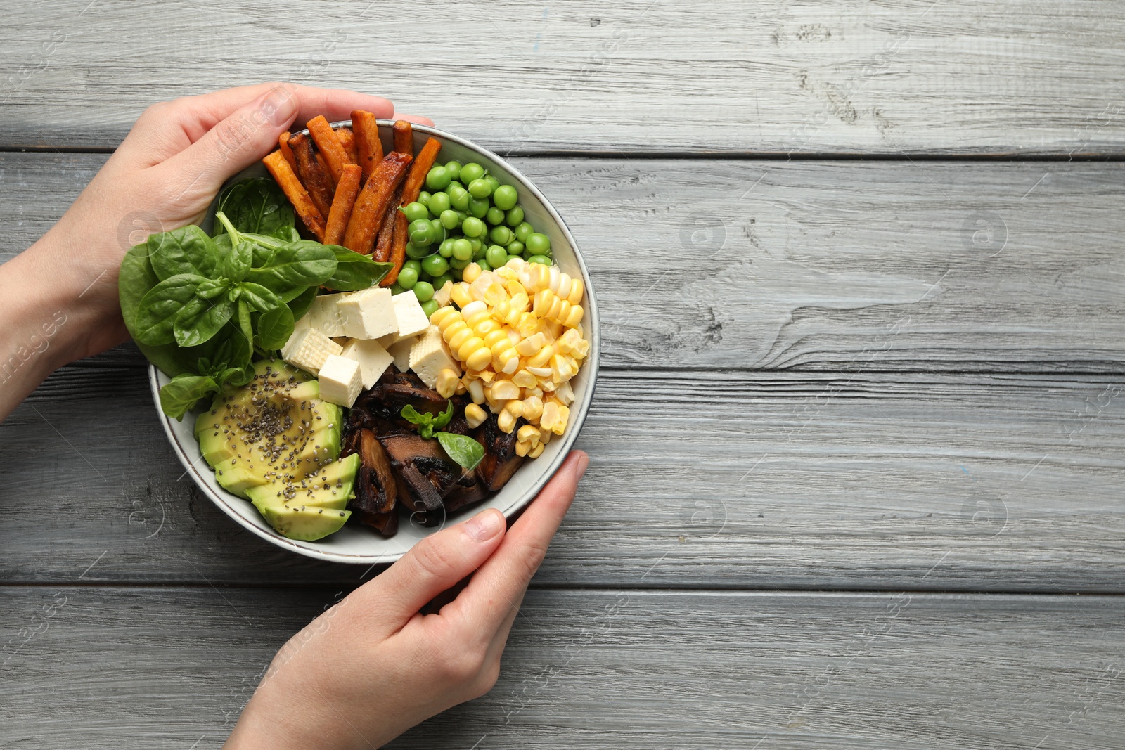 Healthy vegetarian food. Woman with delicious Buddha bowl at grey wooden table, top view. Space for text Photo of Healthy vegetarian food. Woman with delicious Buddha bowl at grey wooden table, top view. Space for text