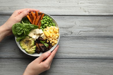 Photo of Healthy vegetarian food. Woman with delicious Buddha bowl at grey wooden table, top view. Space for text