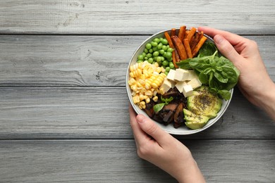 Photo of Healthy vegetarian food. Woman with delicious Buddha bowl at grey wooden table, top view. Space for text