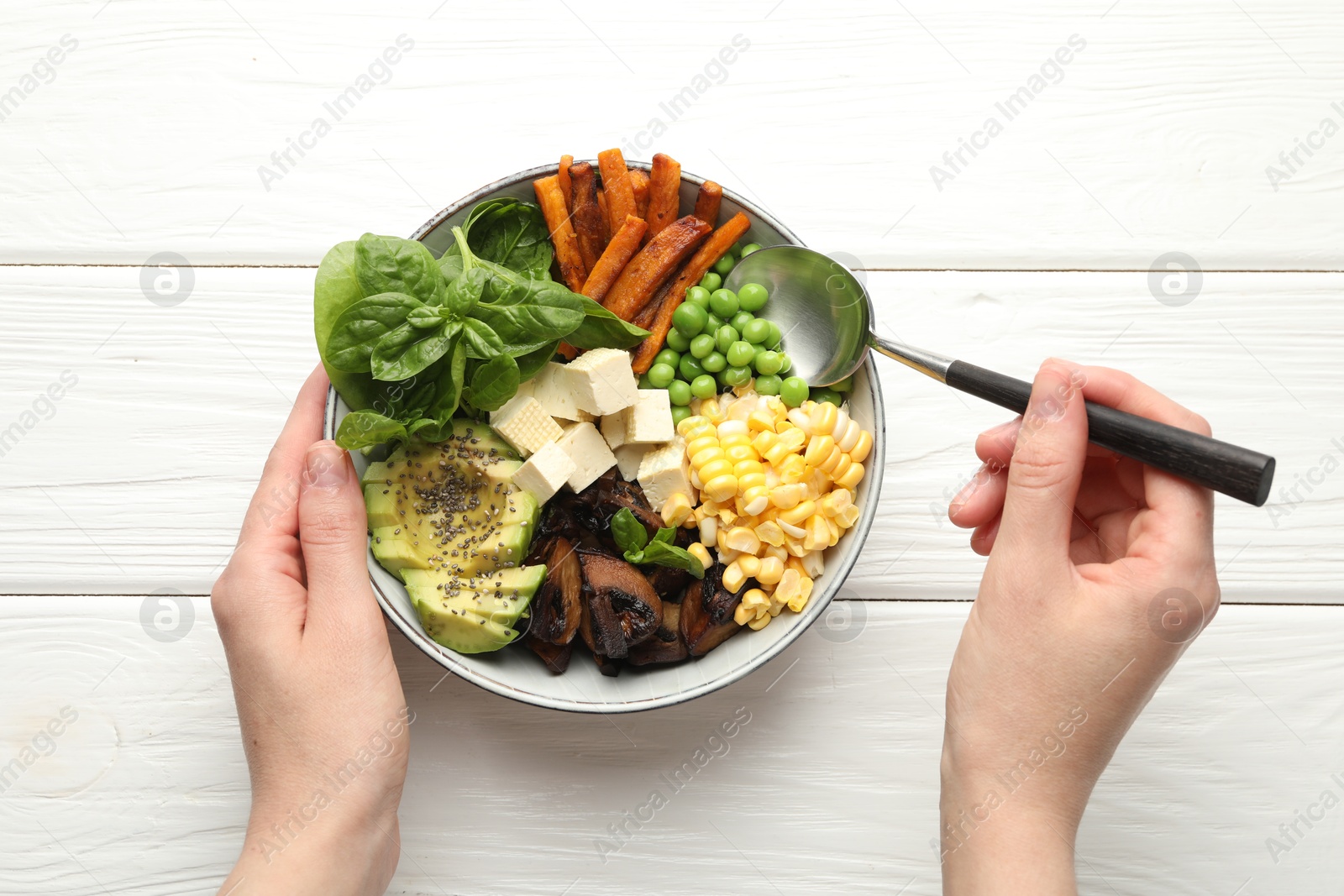 Photo of Healthy vegetarian food. Woman eating delicious Buddha bowl at white wooden table, top view