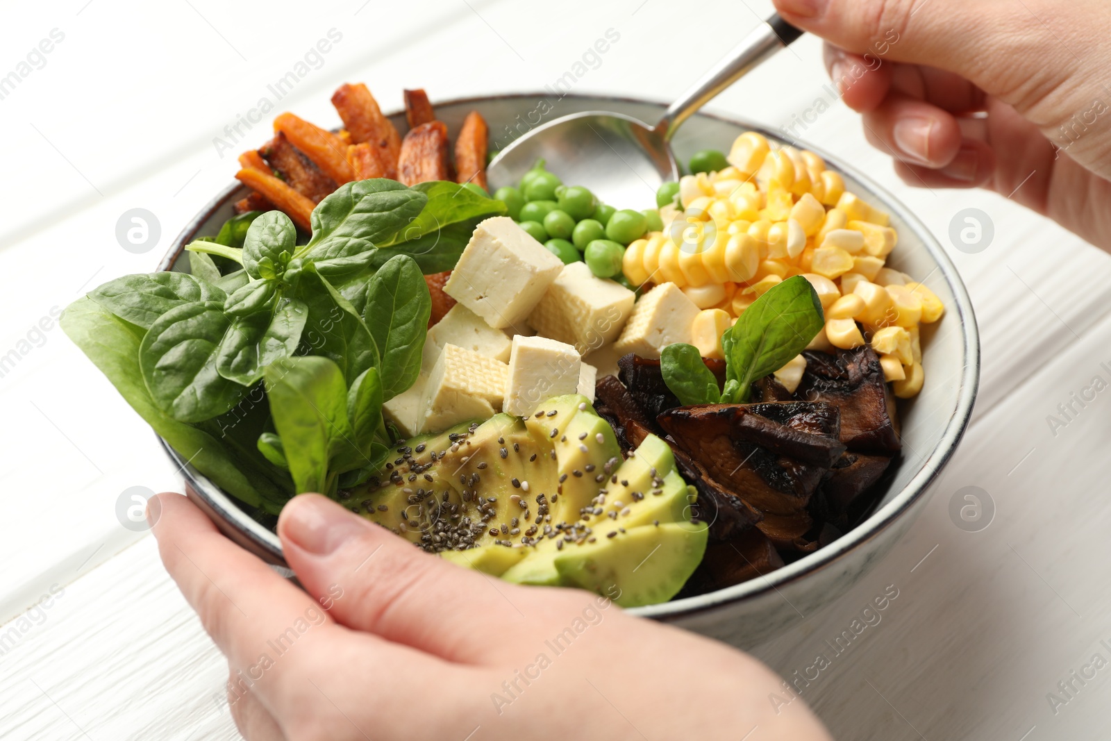 Photo of Healthy vegetarian food. Woman eating delicious Buddha bowl at white wooden table, closeup