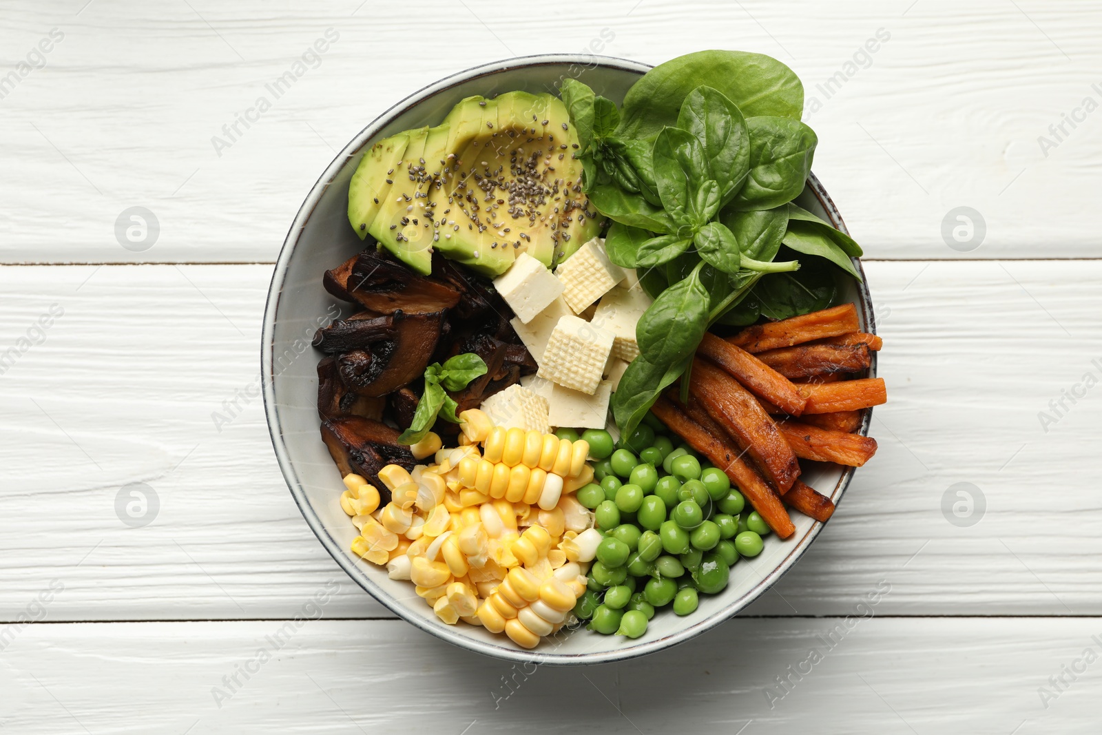 Photo of Healthy vegetarian food. Delicious Buddha bowl with tofu, mushrooms, avocado and vegetables on white wooden table, top view