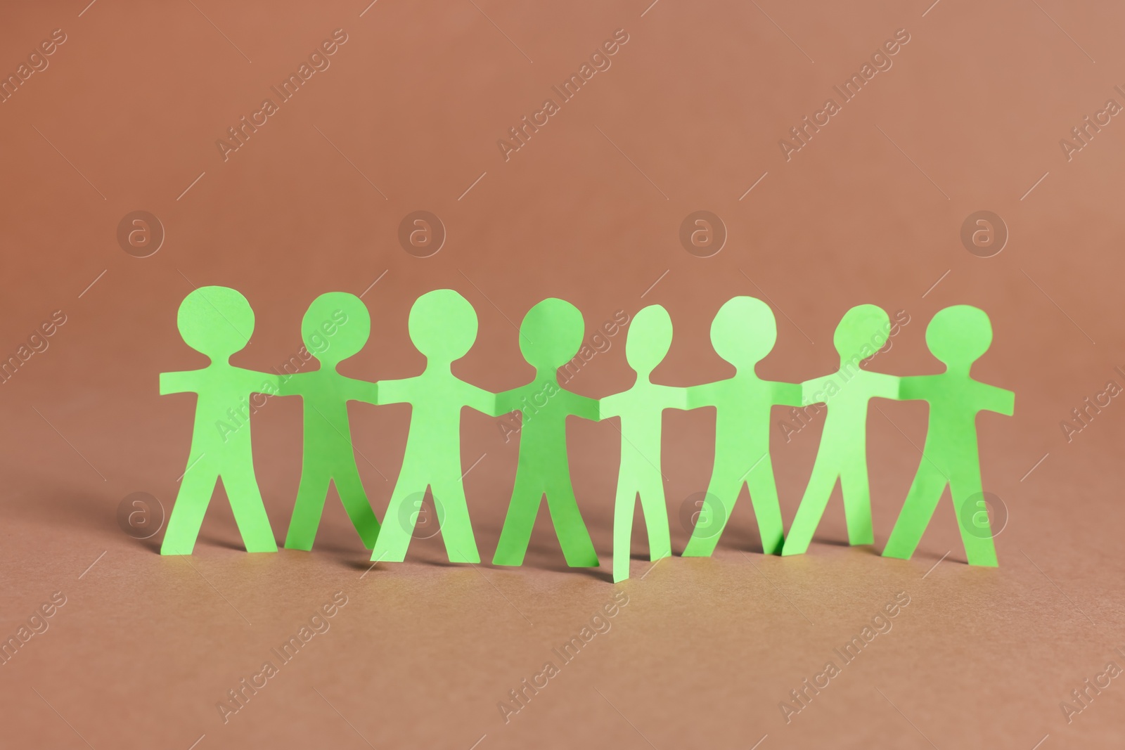 Paper figures of people holding hands on brown background Photo of Paper figures of people holding hands on brown background