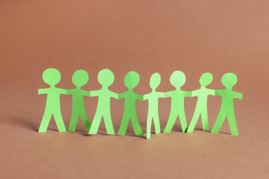 Photo of Paper figures of people holding hands on brown background